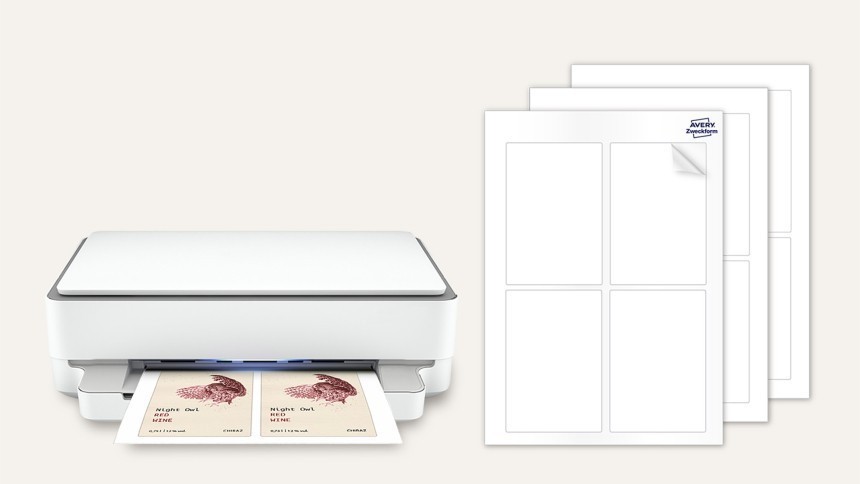 Bílá kancelářská tiskárna vysouvá arch s vytištěnými etiketami s obrázkem sovy, vedle leží tři prázdné archy etiket se čtyřmi prázdnými obdélníky na stránce.