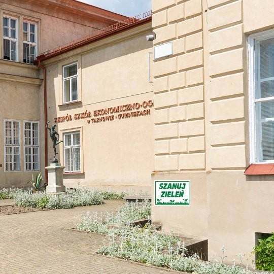 Dům se sochou v popředí a se zelenou značkou na omítce
