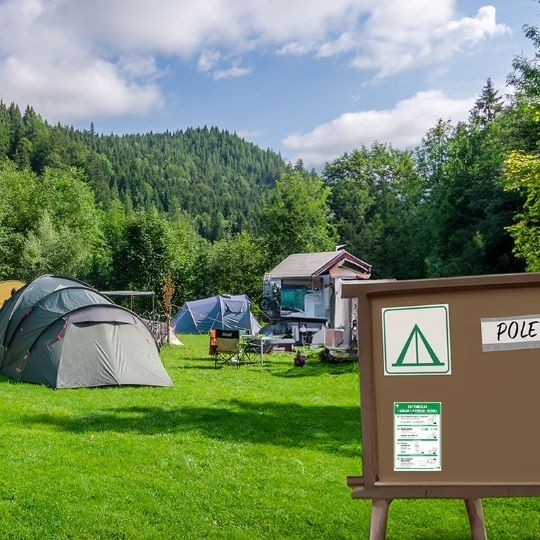 Kemp v přírodě, stany a nástěnka s etiketou značící kemp