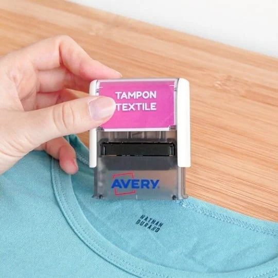 Oděvní známka Avery s nápisem Tampon Textile na růžovém pozadí nalepená na límci zeleného trička