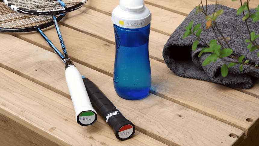 Dřevěný stůl s modrým bidonem a dvěma badmintonovými raketami.