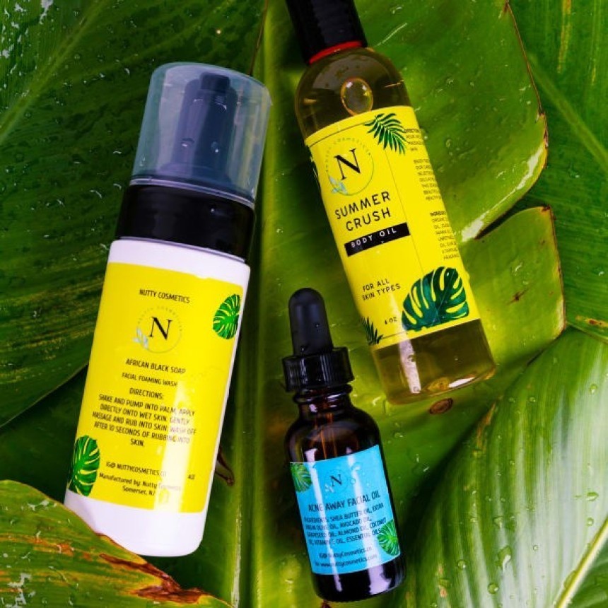 Tři kosmetické přípravky značky "Nutty Cosmetics" ležící na velkém zeleném listu. V sadě se nachází čisticí pěna na obličej, tělový olej a pleťový olej.