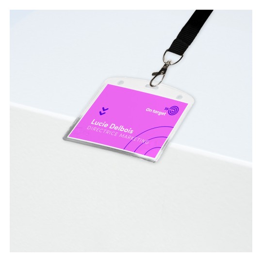 Obrázek ukazuje jmenovku na bílém povrchu. Jmenovka je růžová s jménem 'Lucie Delbois' a titulem 'ŘEDITELKA MARKETINGU'. Je na ní klip připojený k černému popruhu.