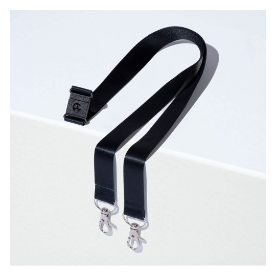 Obrázek zobrazuje černý popruh s klipem na jednom konci a dvěma kovovými klipy na druhém konci, položený na světlém povrchu.