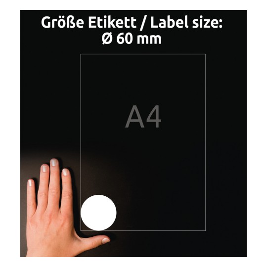 Obraz zobrazuje ruku vedle papíru formátu A4, na němž je v dolním rohu označena velikost štítku o průměru 60 mm, s tmavým pozadím.