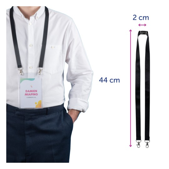 Osoba oblečená v bílé košili stojí s rukama v kapsách a ukazuje jmenovku připevněnou k černé šňůrce. Jmenovka nese jméno 'DAMIEN MIAPING' a slovo 'KOMERČNÍ'. Rozměry šňůrky jsou 44 cm na délku a 2 cm na šířku.