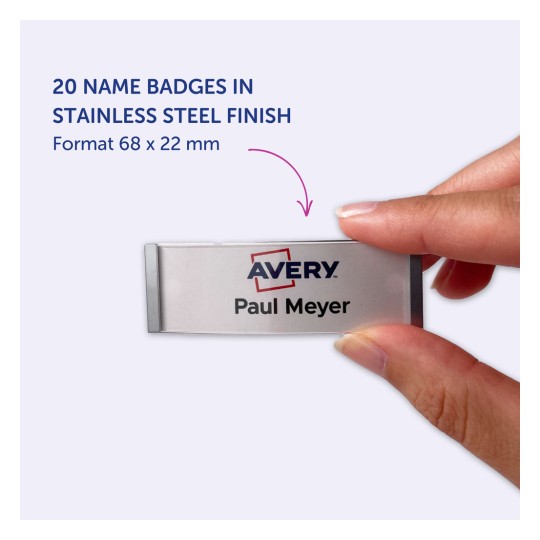 Obrázek zobrazující jmenovku z nerezové oceli s textem 'Avery Paul Meyer'. Jmenovku drží člověk v ruce. Pozadí je světle fialové a rozměry jmenovky jsou uvedeny jako 68 x 22 mm.