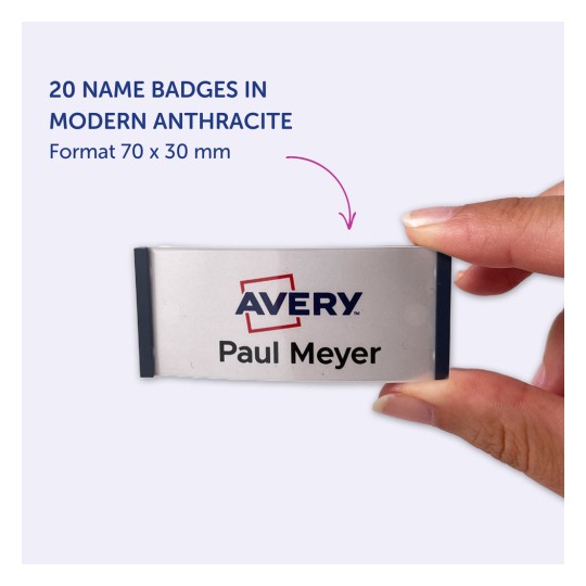 Obrázek ukazuje ruku držící jmenovku označenou 'Avery' se jménem 'Paul Meyer', což naznačuje, že je součástí sady 20 štítků v moderní antracitové barvě, měřících 70 x 30 mm.