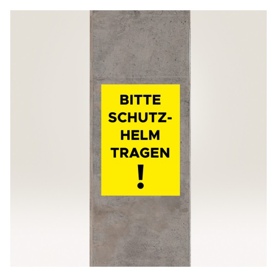 Obrázek zobrazuje žlutou ceduli na betonovém sloupu s nápisem 'BITTE SCHUTZ-HELM TRAGEN!', což se překládá jako 'Prosím, noste helmu!', což naznačuje bezpečnostní požadavek.