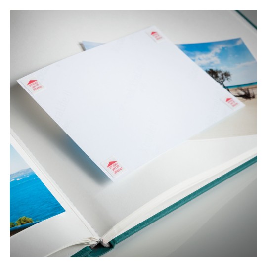 The image shows an open photo album with a blank page and some photos of landscapes. The album has a green spine and the blank page has small labels on the corners.