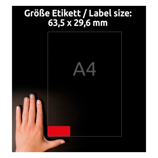 Obrázek zobrazuje ruku vedle listu s etiketami o velikosti A4, přičemž nahoře jsou uvedeny rozměry 63,5 x 29,6 mm. Červená etiketa je zvýrazněna v dolním rohu.