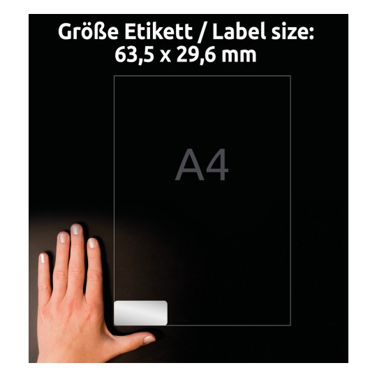 Obrázek zobrazuje ruku, která drží průhledný štítek s textem udávajícím velikost štítku 63,5 x 29,6 mm, vedle odkazu na formát papíru A4.