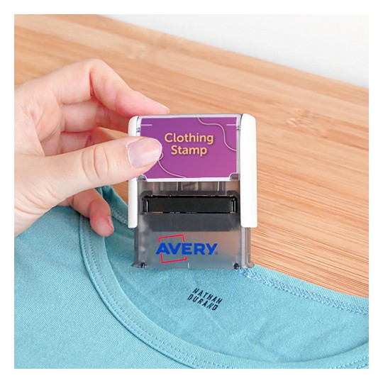 Obrázek zobrazuje osobu držící razítko na oblečení, které je umístěno nad košilí. Na razítku je označení 'Clothing Stamp' a viditelný název značky 'Avery'.
