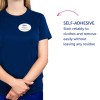 Obrázek ukazuje osobu, která má na sobě modrou košili se jmenovkou s nápisem 'B. Carlos, Marketingový ředitel.' Vedle nich je text popisující samolepicí funkci, která se lepí na oblečení a lze ji snadno odstranit bez zanechání zbytku.