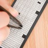 Obrázek ukazuje ruku, která používá pinzetu k vybírání písmen z řady malých bílých plastových dlaždic uspořádaných v řadách, s dřevěným povrchem pod nimi.