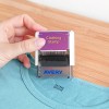 Obrázek zobrazuje osobu držící razítko na oblečení, které je umístěno nad košilí. Na razítku je označení 'Clothing Stamp' a viditelný název značky 'Avery'.